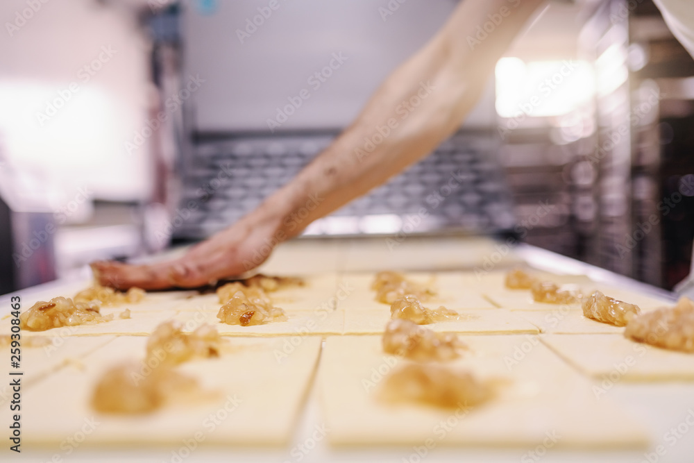 Fototapeta premium Caucasian hardworking baker making rolls with jam. Bakehouse interior.