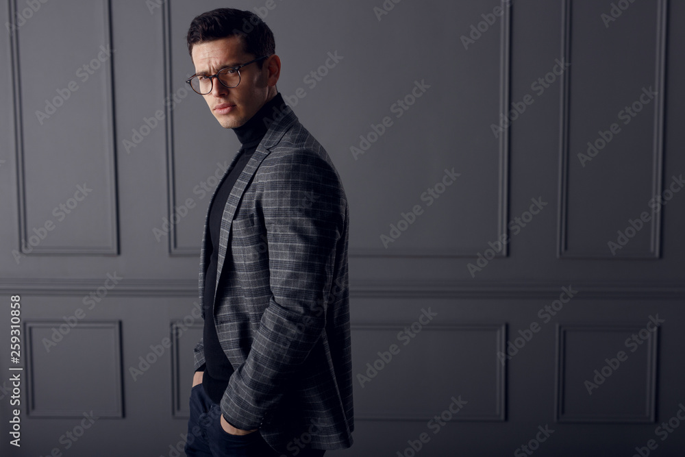 Handsome young brunette model, wearing in grey jacket, looking with attitude, isolated on grey background. Copy space.