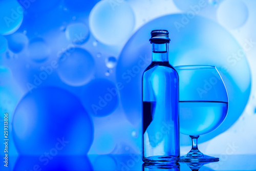 transparent glass and bottle with water and oily drops on azure background 
