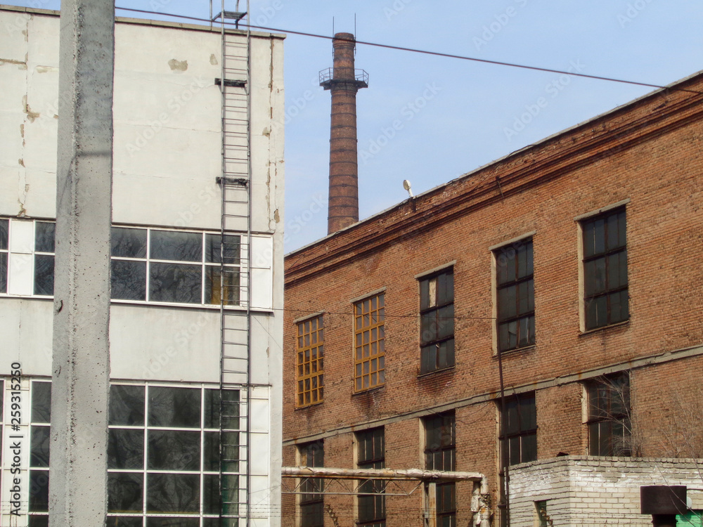 Old industrial buildings with concrete and red brick facades. Ust-Kamenogorsk (Kazakhstan). Factory chimney. Industrial area