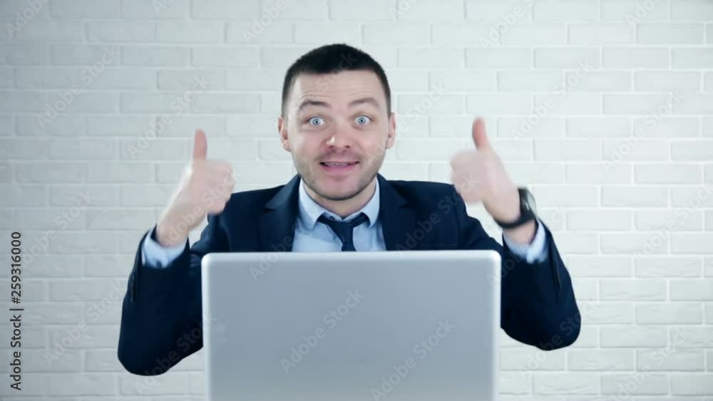 Businessman showing thumbs up while using laptop in office Businessman showing thumbs up while using laptop in office