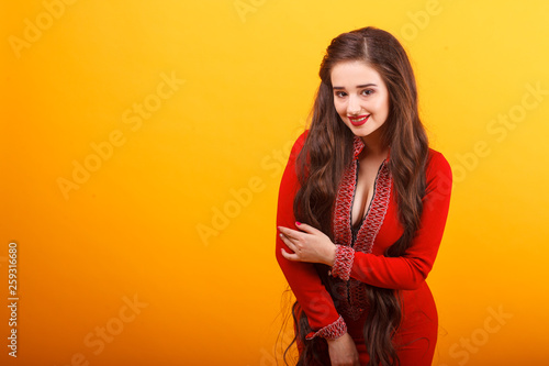 Beautiful young woman in red mini dress. Studio shot on yellow background.