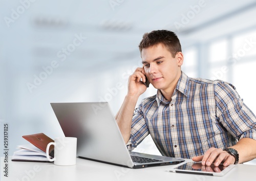 Happy young man works on his laptop with coffee at the table