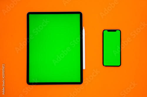 new tablet on a Orange background with a keyboard and pen, and green screen top view