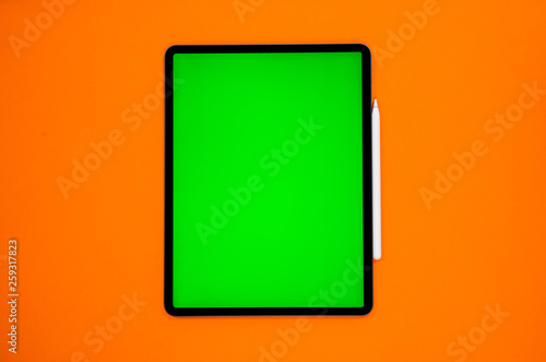 new tablet on a Orange background with a keyboard and pen, and green screen top view