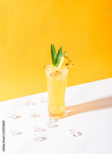 iced pineapple punch cocktail in glass on yellow background. summer drink.