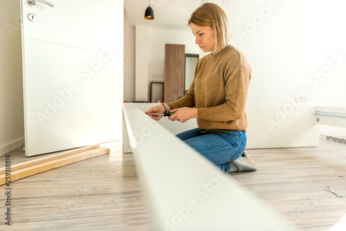 Young woman assembling furniture in new house 