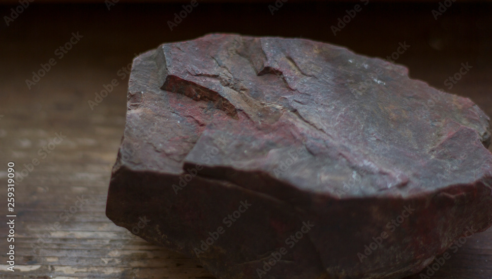 close-up a beautiful piece of raw red-brown jasper lies on a dark windowsill