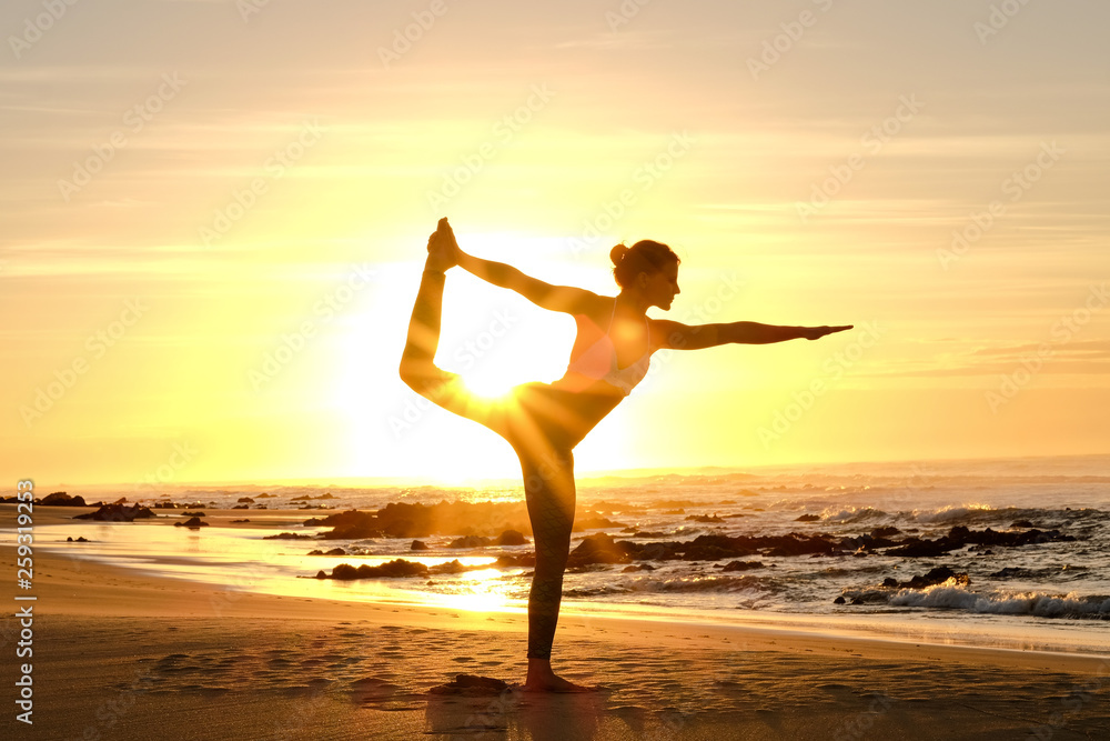 An awesome yoga instructor does some poses on the beach with the sunrise