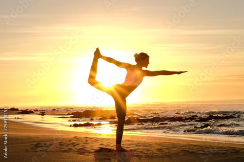 An awesome yoga instructor does some poses on the beach with the sunrise