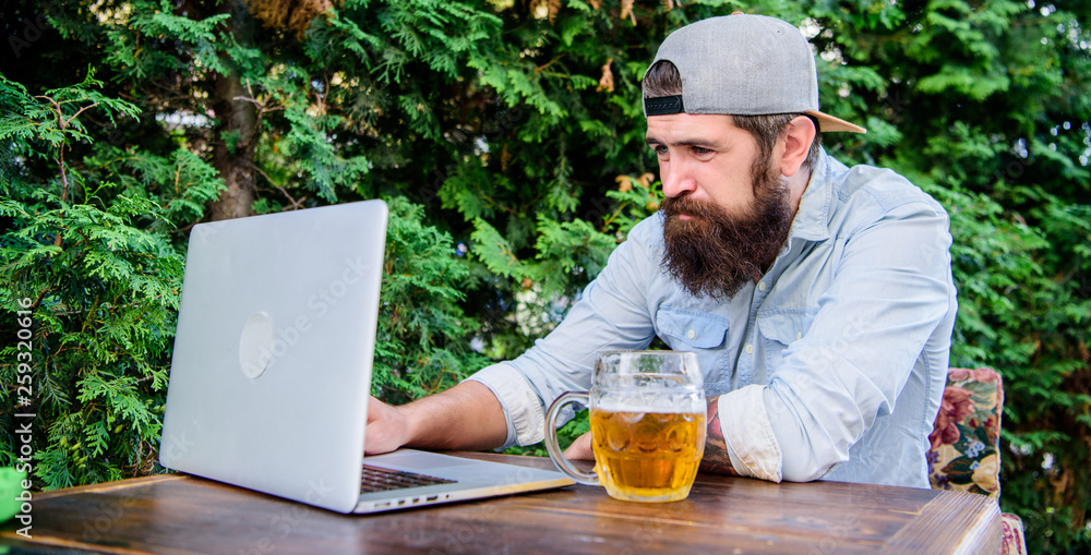 Using new technology. Bearded man communicating through communication technology. Hipster drinking beer and using laptop technology in outdoor cafe. Remaining productive with computer technology Using new technology. Bearded man communicating through communication technology. Hipster drinking beer and using laptop technology in outdoor cafe. Remaining productive with computer technology