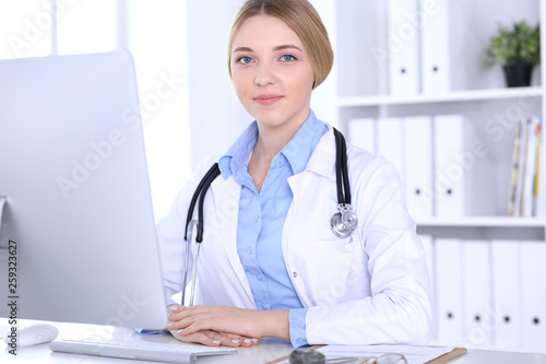 Young woman doctor at work in hospital looking at desktop pc monitor. Physician controls medication history records and exam results. Medicine and healthcare concept