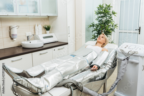 Quadro su tela Blonde girl lying on beauty couch during pressotherapy session in clinic