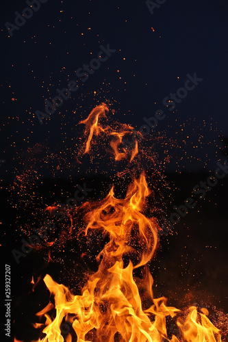 Flame of a burning campfire with sparks against a dark blue sky. Close-up