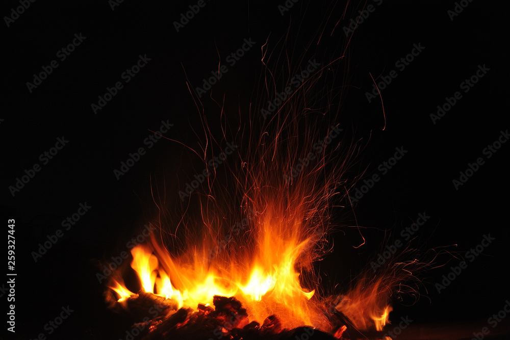 Flame of a burning fire with sparks in the night on a black background. Close-up