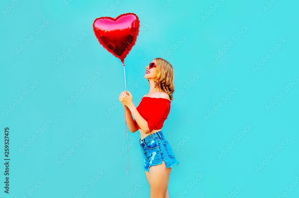 Portrait happy smiling woman looking at red heart shaped air balloon on colorful blue background Portrait happy smiling woman looking at red heart shaped air balloon on colorful blue background