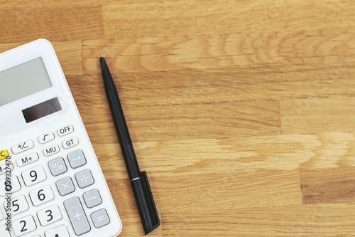 top view of black pen with calculator on vivid office desk table wooden background table for business with blank copy space, math, cost, tax or investment calculation.