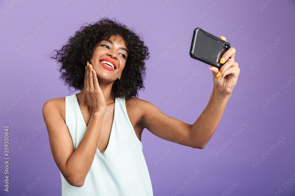 Naklejka premium Smiling pretty african woman making selfie and touching her cheek