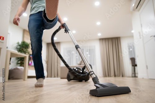 Wide angle photo of woman housewife or maid or service worker hoovering with vacuum cleaner in bright luxury appartment.