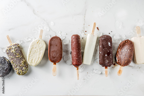 Assortment of various popsicle ice cream, vanilla and chocolate, with nuts, on a dark concrete background with ice, copy space top view photo