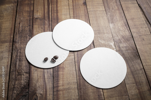 Three blank beer coasters and coffee beans on wooden background. Responsive design mockup.