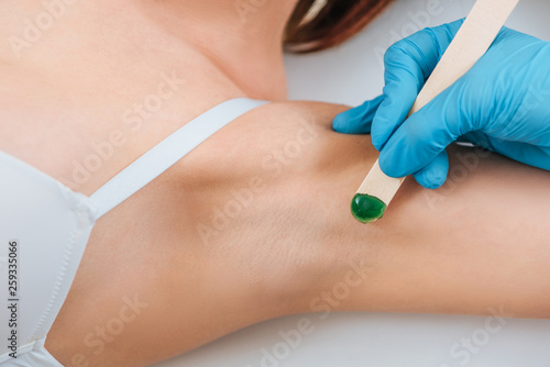 Cropped view of cosmetologist using putty knife for armpit wax depilation