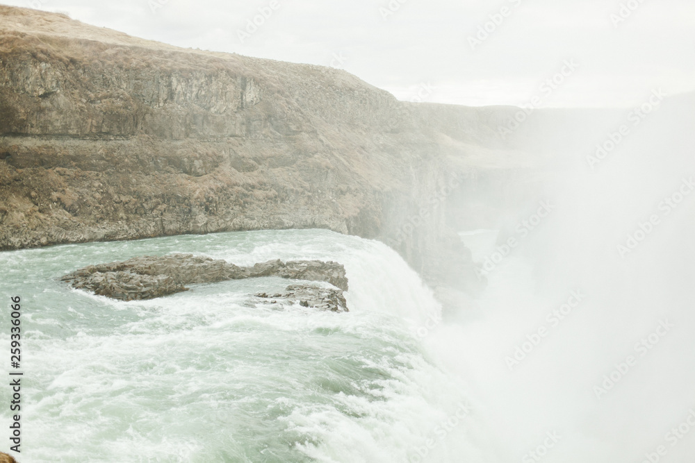 View of a large waterfall in Iceland. June summer day near the raging mountain river and waterfall View of a large waterfall in Iceland. June summer day near the raging mountain river and waterfall
