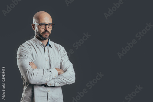 Serious middle aged man with a deadpan face expression dressed in casual posing on a dark gray background