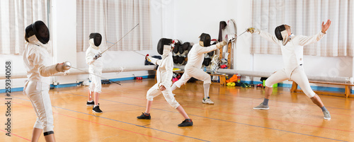 Adults and teens wearing fencing uniform practicing with foil photo