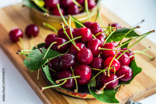 A handful of ripe red cherries in a metal can on a white background with green leaves
