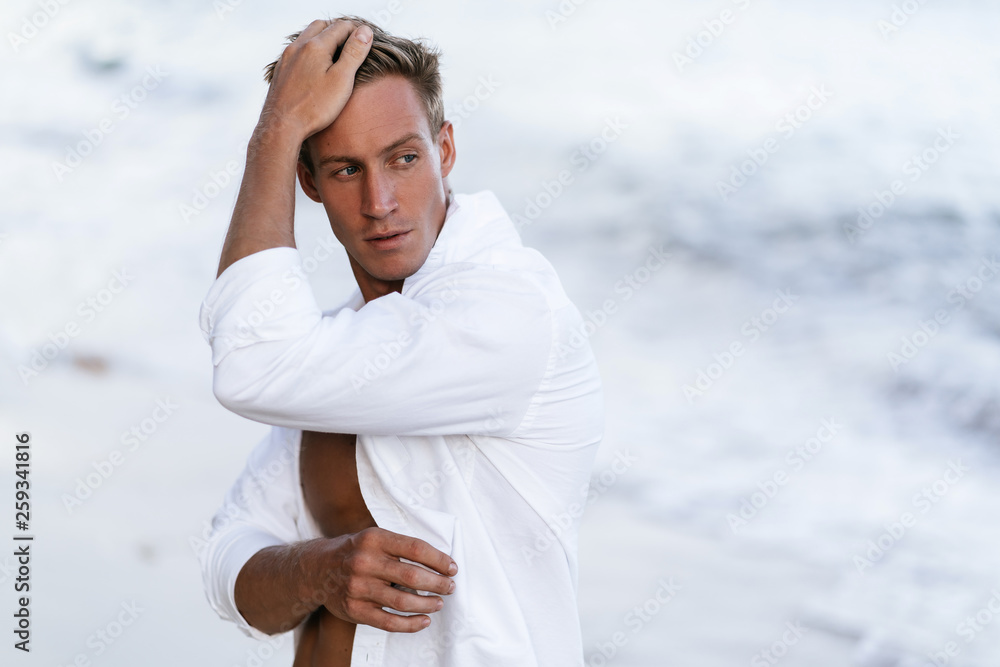 Portrait of handsome sexy man in white shirt posing on beach, ocean waves  at background Stock Photo | Adobe Stock