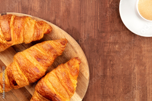 A closeup of a breakfast with croissants and coffee  shot from above forming a frame on a dark rustic wooden background with copy space