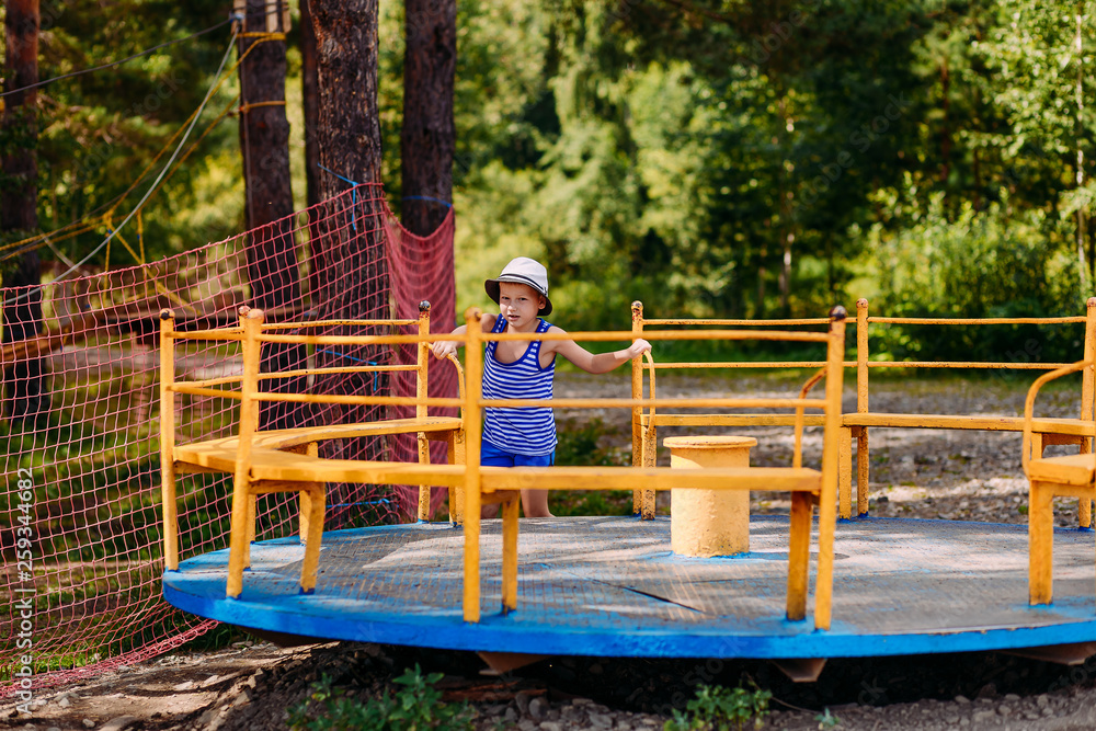 seven-year-old boy in a hat spins a big carousel in summer seven-year-old boy in a hat spins a big carousel in summer