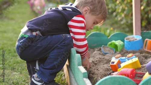 Little toddler boy playing in sandbox on playground in sunny day