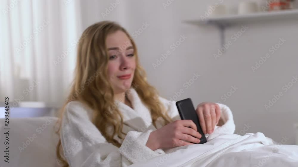 Crying woman in bed typing message on smartphone, quarrelling with boyfriend Crying woman in bed typing message on smartphone, quarrelling with boyfriend