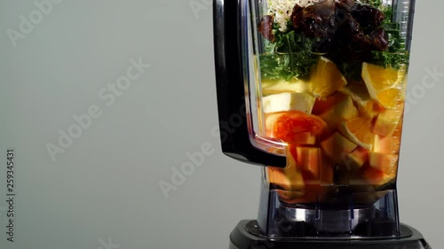 Making fresh fruits cocktail shake. Papaya, banana slices, curly kale leaves and sprouts in blender ready to be mixed, machine rotating on grey, text area. Healthy food, dieting photo