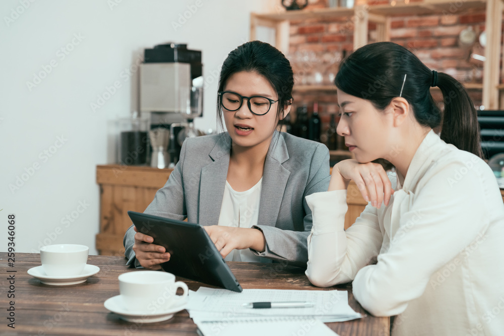 female graphic designer pointing with finger on tablet pc during collaboration with office colleague on common project in coffee shop. Two businesswomen discussing website on digital pad in cafe. female graphic designer pointing with finger on tablet pc during collaboration with office colleague on common project in coffee shop. Two businesswomen discussing website on digital pad in cafe.