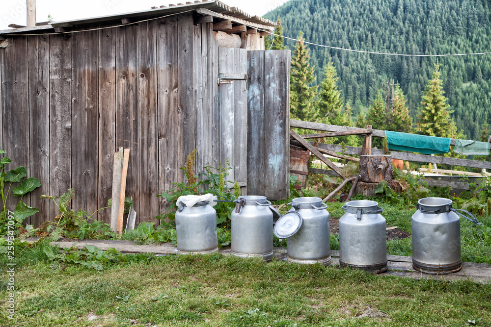 buckets of milk are on the background of the mountains and a wooden shed buckets of milk are on the background of the mountains and a wooden shed
