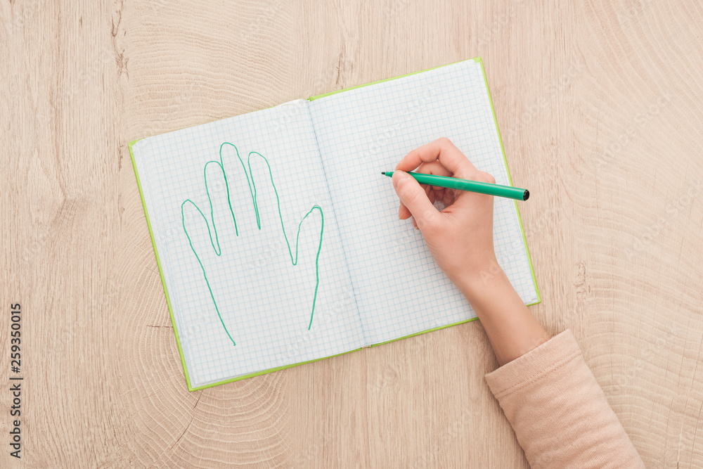cropped view of female hand on opened notebook near drawn human palm cropped view of female hand on opened notebook near drawn human palm