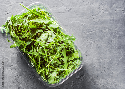 Fresh green arugula leaves in a plastic package box on Dark grey black slate background with copy space. top view