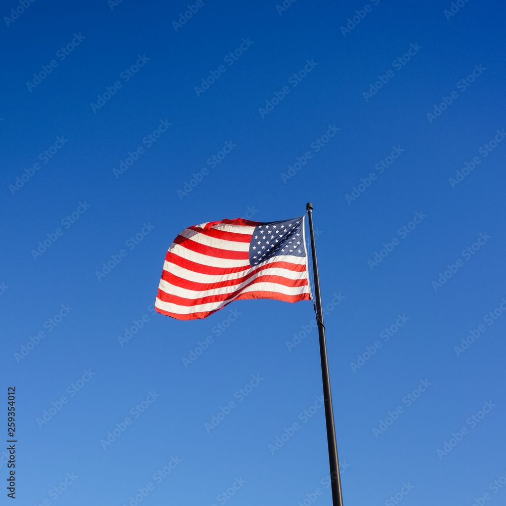 Square image of national flag of the United States of America, also called Stars and Stripes, Old Glory or Star-Spangled Banner waving on July 4th in the wind and sunlight against clear blue sky Square image of national flag of the United States of America, also called Stars and Stripes, Old Glory or Star-Spangled Banner waving on July 4th in the wind and sunlight against clear blue sky