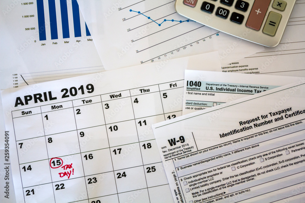 Top view of desk with calculator, tax forms, graphs and calendar sheet with tax date marked