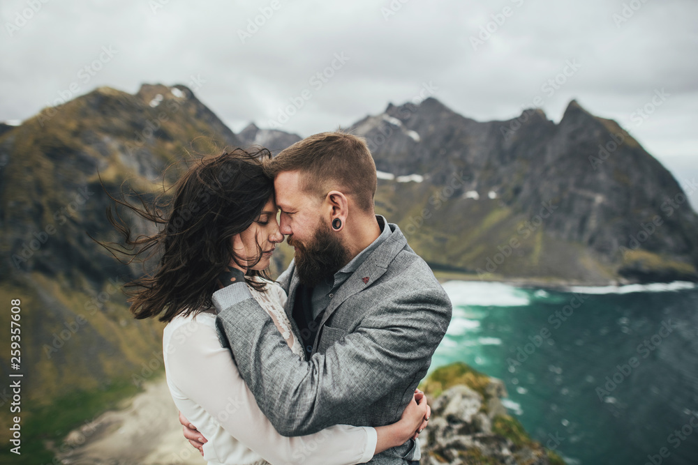 Naklejka premium Wedding couple travelers on a hill in Norway, Kvalvika. Beautiful view of the beach, Lofoten, Norway.