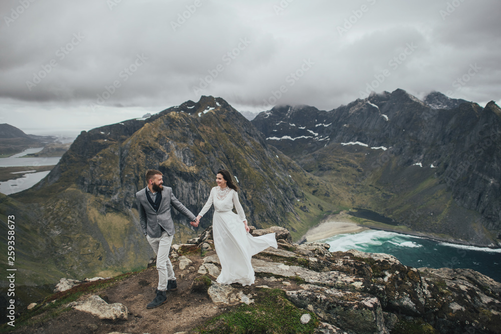 Fototapeta premium Wedding couple travelers on a hill in Norway, Kvalvika. Beautiful view of the beach, Lofoten, Norway.