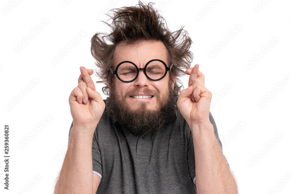 © DenisNata - Crazy Bearded happy Man with funny Haircut in Eyeglasses making Luck gesture. Cheerful and silly guy crossing his fingers, isolated on white background.