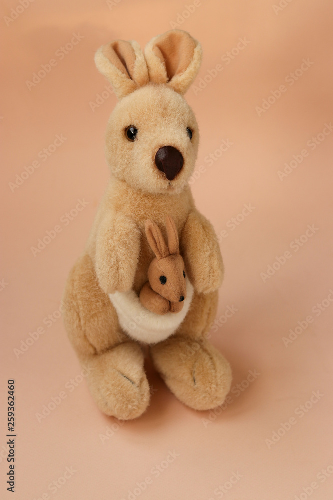 Soft toy mom kangaroo with a baby is located on a peach background, vertical Soft toy mom kangaroo with a baby is located on a peach background, vertical