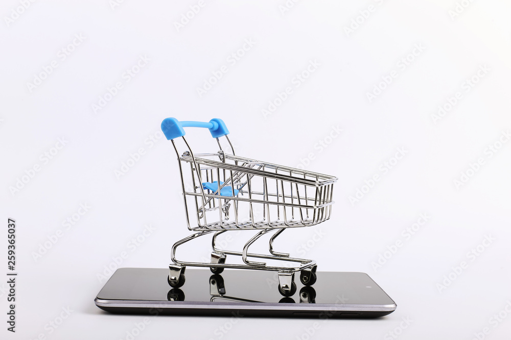 Shopping cart stands on the smartphone. Online sales concept.
