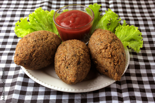 kibbeh fried with tomato sauce on a plate, on table lined with checkered tablecloth photo