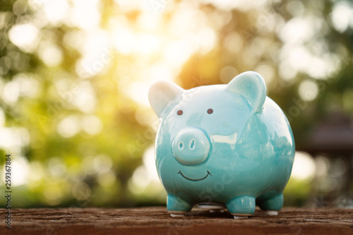 Blue piggy bank on wooden table over blurred green bokeh background. Saving money concept