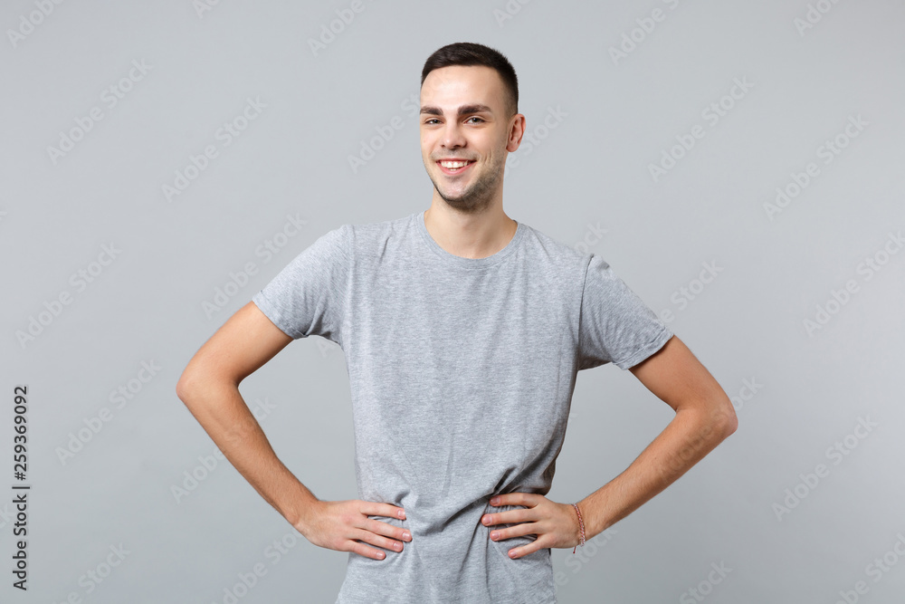 Portrait of smiling handsome young man in casual clothes standing with arms akimbo on waist isolated on grey wall background in studio. People sincere emotions, lifestyle concept. Mock up copy space. Portrait of smiling handsome young man in casual clothes standing with arms akimbo on waist isolated on grey wall background in studio. People sincere emotions, lifestyle concept. Mock up copy space.